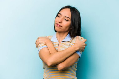 Genç İspanyol kadın mavi arka planda yalnızdı. Kucaklaşma, kaygısız gülümseme ve mutluluk..