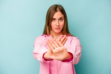 Mavi arka planda izole edilmiş genç beyaz kadın elini uzatmış, dur işareti göstererek seni engelliyor..