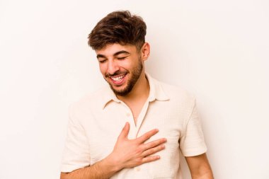 Beyaz arka planda izole edilmiş genç İspanyol adam yüksek sesle gülüyor elini göğsüne koyuyor..