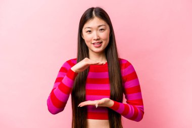 Pembe arka planda izole edilmiş genç Çinli kadın iki eliyle bir şey tutuyor, ürün sunumu..