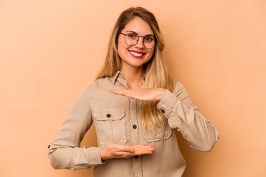 Beyazlı genç bir kadın bej arka planda izole edilmiş iki eliyle bir şey tutuyor, ürün sunumu.