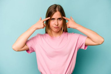 Kafkasyalı genç bir kadın mavi arka planda izole edilmiş bir vazifeye odaklanmış, parmaklarını işaret ediyor..