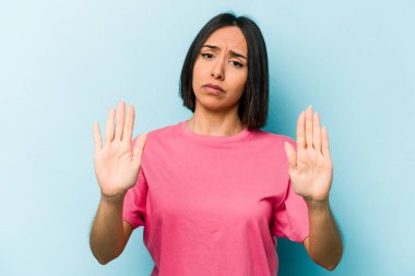 Mavi arka planda izole edilmiş genç İspanyol kadın elini uzatmış, dur işareti göstererek seni engelliyor..