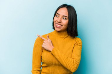 Mavi arka planda soyutlanmış genç İspanyol kadın gülümseyen, neşeli ve keyifli bir kenara bakıyor..