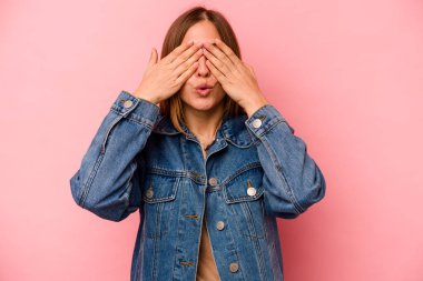 Pembe arka planda izole edilmiş genç beyaz kadın elleriyle gözlerini kapatmaktan korkuyor..