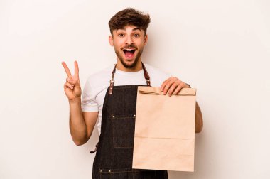 Beyaz arka planda, neşeli ve tasasız bir şekilde izole edilmiş bir çanta taşıyan genç İspanyol tezgahtar parmaklarıyla barış sembolü gösteriyordu..