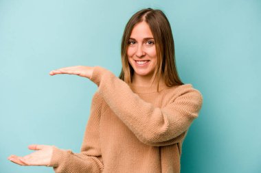 Kafkasyalı genç bir kadın mavi arka planda izole edilmiş. Elinde parmakları olan, gülümseyen ve kendinden emin bir şey var..