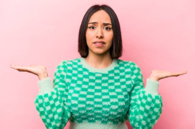 Pembe arka planda izole edilmiş genç İspanyol kadın. Kopya alanını tutmak için kafası karışık ve omuz silkiyor..