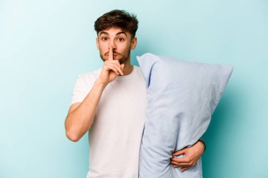 Mavi arka planda izole edilmiş pijama giyen genç İspanyol bir adam bir sır saklıyor ya da sessizlik istiyor..