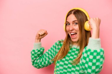 Pembe arka planda müzik dinleyen beyaz bir kadın zafer kazandıktan sonra yumruğunu kaldırıyor..
