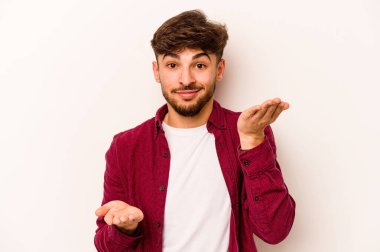 Beyaz arka planda izole edilmiş genç İspanyol adam kollarıyla ölçeği yapıyor, mutlu ve kendinden emin hissediyor..