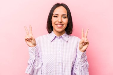 Pembe arka planda izole edilmiş genç İspanyol kadın zafer işareti gösteriyor ve gülümsüyor..
