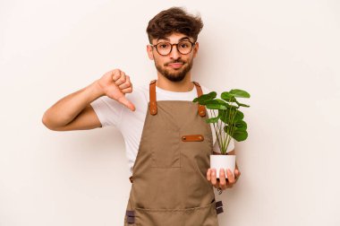 Genç bahçıvan İspanyol bir adam beyaz arka planda izole edilmiş bir bitki tutuyor. Sevimsiz bir jest gösteriyor. Anlaşmazlık konsepti.