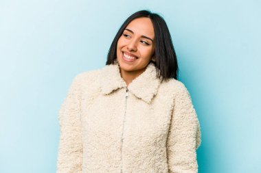 Mavi arka planda izole edilmiş genç İspanyol kadın gülüyor ve gözlerini kapıyor, rahatlamış ve mutlu hissediyor..