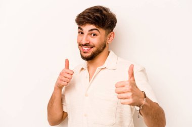 Beyaz arka planda izole edilmiş genç bir İspanyol. Baş parmağını kaldırıyor, gülümsüyor ve kendinden emin..