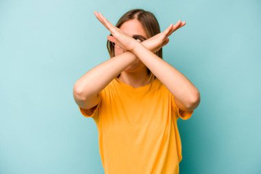 Mavi arka planda izole edilmiş genç beyaz kadın iki kolu çapraz tutuyor, inkar kavramı.