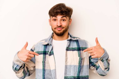 Beyaz arka planda izole edilmiş genç bir İspanyol gömlek fotokopi alanını elle işaret ediyor, gururlu ve kendinden emin.