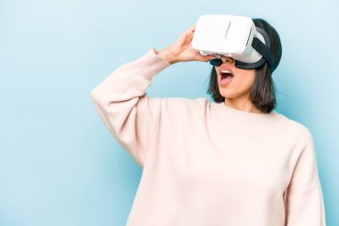 Mavi arka planda izole edilmiş sanal gözlük takan genç İspanyol kadın.