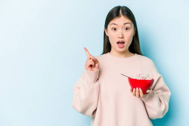 Genç Asyalı bir kadın elinde bir kase mısır gevreği tutuyor. Mavi arka planda, yan tarafı işaret ediyor.