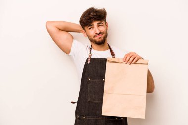 Beyaz arka planda izole edilmiş bir çanta taşıyan genç İspanyol tezgahtar başının arkasına dokunup düşünüyor ve bir seçim yapıyor..