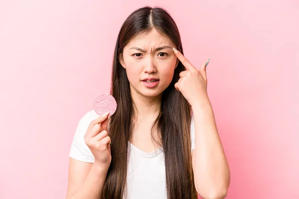 年轻的亚洲女人手握粉红背景的面部海绵 用食指表现出失望的姿态 — 图库照片