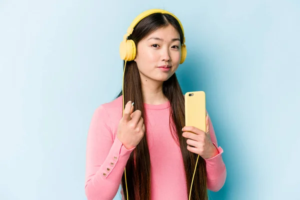 Jovem Mulher Asiática Ouvindo Música Isolada Fundo Azul Apontando Com — Fotografia de Stock