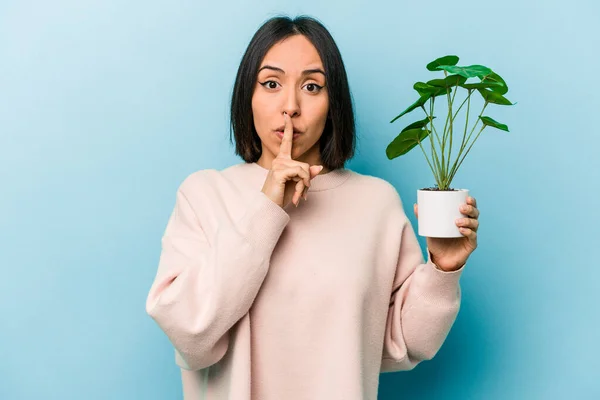 Jovem Hispânica Segurando Uma Planta Isolada Fundo Azul Mantendo Segredo — Fotografia de Stock