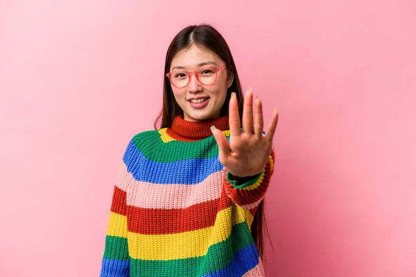 Pembe arka planda izole edilmiş genç Çinli bir kadın gülümseyerek beş numarayı parmaklarıyla gösteriyor..
