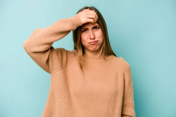 Mavi arka planda izole edilmiş genç beyaz kadın şakaklara dokunuyor ve baş ağrısı çekiyor..