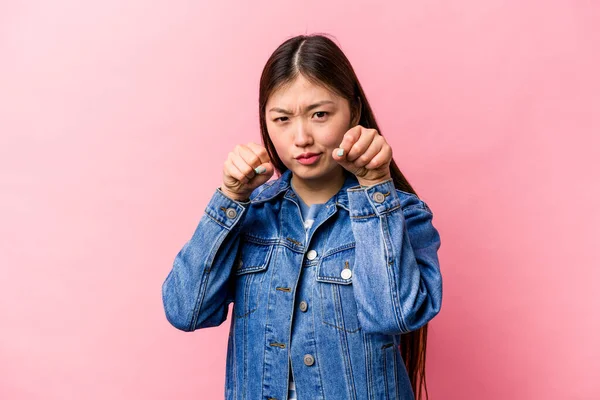 Young Chinese woman isolated on pink background throwing a punch, anger, fighting due to an argument, boxing.