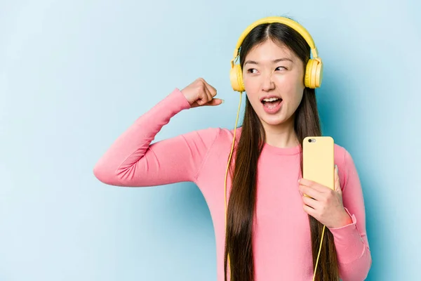 Jovem Mulher Asiática Ouvindo Música Isolada Fundo Azul Levantando Punho — Fotografia de Stock