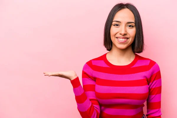 ピンクの背景に孤立した若いヒスパニック系の女性は 手のひらにコピースペースを示し 腰に別の手を保持 — ストック写真