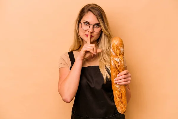 Young caucasian baker woman isolated on beige background keeping a secret or asking for silence.