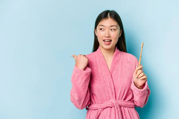 年轻的亚洲女人穿着浴衣刷牙 用粉红的背景点隔开 无忧无虑地笑着 无忧无虑 — 图库照片