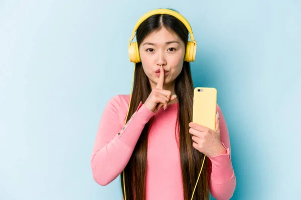 Jovem Mulher Asiática Ouvindo Música Isolada Fundo Azul Mantendo Segredo — Fotografia de Stock