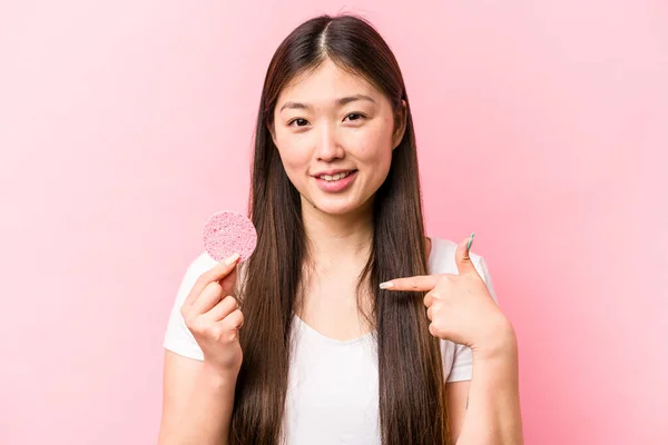 年轻的亚洲女人 手里拿着用粉红背景的海绵 手指着衬衫的复制品空间 自豪而自信 — 图库照片