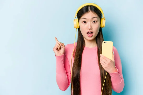 Jovem Mulher Asiática Ouvindo Música Isolada Fundo Azul Apontando Para — Fotografia de Stock