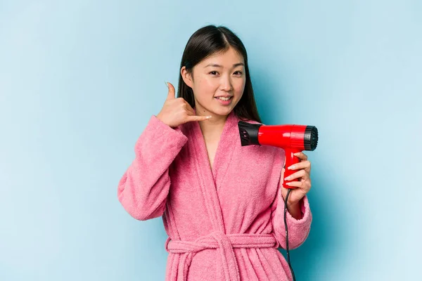 年轻的亚洲女人穿着浴衣 手握粉色背景的吹风机 手握手指 摆出手机手势 — 图库照片