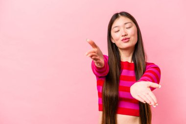 Pembe arka planda izole edilmiş genç Çinli bir kadın. Dudakları kıvrılmış, avuç içleri havada öpüşmek için tutulmuş..