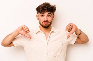 Beyaz arka planda izole edilmiş genç İspanyol adam baş parmağını aşağı gösteriyor, hayal kırıklığı konsepti..