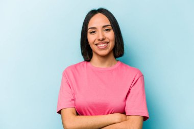Mavi arka planda kendini güvende hisseden, kararlılıkla kollarını kavuşturan genç İspanyol kadın..