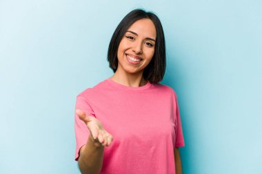 Mavi arka planda izole edilmiş genç İspanyol kadın selamlaşmak için kameraya elini uzatıyor..