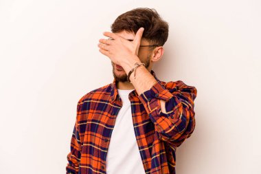 Beyaz arka planda izole edilmiş genç İspanyol adam elleriyle gözlerini kapatıyor, geniş bir gülümsemeyle bir sürpriz bekliyor..