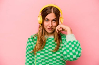 Pembe arka planda izole edilmiş müzik dinleyen beyaz bir kadın şakağı parmağıyla işaret ediyor, düşünüyor ve bir göreve odaklanıyor..