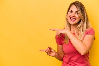 Sarı arka planda izole edilmiş genç beyaz kadın işaret parmağıyla işaret ederek heyecanlanıyor..