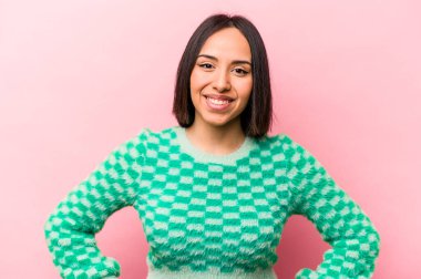 Pembe arka planda izole edilmiş genç İspanyol kadın ellerini kalçasında tutuyor..