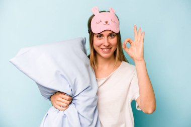 Mavi arka planda izole edilmiş pijama giyen beyaz bir kadın. Neşeli ve kendinden emin..