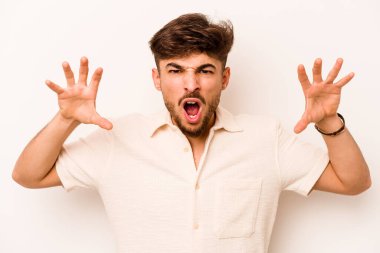 Beyaz arka planda izole edilmiş genç İspanyol bir adam pençelerini bir kediyi taklit ederken gösteriyor, agresif bir hareket..