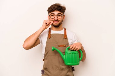 Genç bahçıvan İspanyol bir su bidonu tutuyor beyaz arka planda, parmakları dudaklarında bir sır saklıyor..