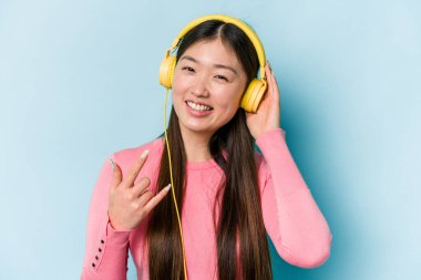 Genç Asyalı kadın mavi arka planda izole edilmiş müzik dinliyor.